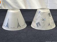 Two conical glass lampshades with black and blue Paris themed prints, showing Eiffel Tower and other Parisian motifs.