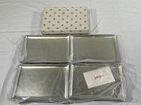 Four rectangular metal trays arranged with original packaging and Neiman Marcus branded card visible.