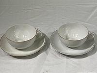 Two white hand painted Nippon teacups with matching saucers placed side by side on a white background, showing size and shape.