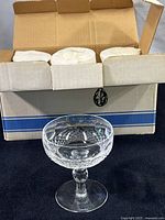 Photo of open cardboard box with white internal packaging and one crystal glass in front, showing the packaging setup and a full view of the glass.