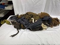 Bundle of wool yarn in various earthy gradient colors laid on white fabric for color and texture display.