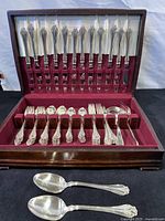 Full view of cutlery set in wooden case with burgundy velvet slots holding knives, forks, and spoons neatly arranged