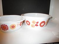 Front view of two white glass bowls with colorful retro floral patterns on the sides, showing their size difference and pattern detail.
