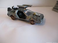 Side view of silver 1/32 scale die-cast DeLorean model with gull-wing doors open, showing details of interior and engine components on hood.