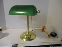 Front view of brass bankers lamp with green glass shade, showing brass base, pole, and pull chain