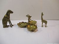 Full view of three brass items including dog figurine, giraffe figurine, and three-compartment serving tray with angel figurine on a white surface.