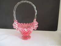 Front view of cranberry hobnail opalescent glass basket with clear handle against black background
