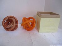 Two glass endless knot ornaments displayed side by side with box in background.