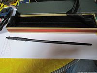 Black wand with textured handle laying next to open presentation box with black velvet interior