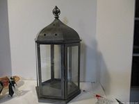 Front view of large hexagonal metal and glass candle holder on a white surface showing detailed metalwork and glass panels.