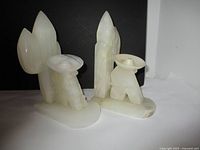 Photo of two white marble bookends showing abstract figures sitting next to cactus shapes on dark background.
