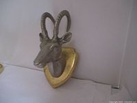Side angle view of metal deer head wall ornament showing texture and gold shield backing.