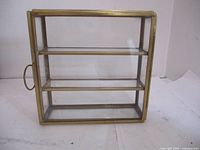 Front and side view of the vintage display case showing clear glass panels and brass framing with three internal shelves and a brass handle on the side.