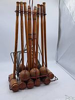 Front view of wooden croquet mallets and balls stored in red metal rack showing condition