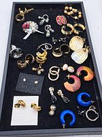 Photo showing a tray filled with assorted costume jewellery including various earrings and brooches of different styles and colors.