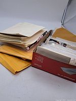 Photo of assorted envelopes and paper sheets contained in a box and stacked beside it showing vintage used condition.