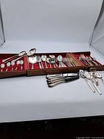 Full display of the flatware set in an open wooden canteen with red velvet lining, showing a variety of spoons, forks, and other utensils.