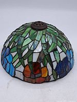 Side view of the dome-shaped coloured leaded glass lampshade showing blue and orange flowers with green and white leaves.