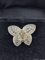 Front view of gold-tone butterfly brooch decorated with clear rhinestones on a black fabric background.
