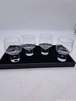 Four rounded bowl glasses with thick cylindrical bases on a black tray