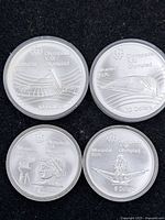 Four silver coins in protective capsules arranged on black mat, showing all obverse designs