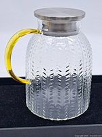 Front view of the glass pitcher showing the textured surface and yellow handle with metal lid on top.