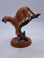 Full side view of the hand-painted bisque porcelain cougar figurine perched on a tree branch, showing the wooden base.
