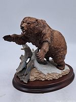Full view of the grizzly bear figurine on wooden base, showing bear in a dynamic stance with one paw raised and textured base.