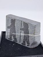 Front view showing two Inuit figures walking with sticks carved into gray soapstone slab.