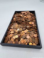 Loose pennies in a black tray, mixed Canadian and US coins, showing circulated condition and patina.