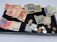 Photo showing spread of mixed coins and worn paper money on black surface.