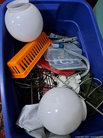 Blue Rubbermaid tote showing frosted glass globe light fixtures, orange tool holder, electrical cords and other items