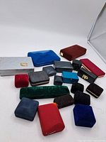 Top-down view of 18 assorted vintage jewellery cases in various colors and materials arranged on white surface.