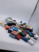 Wide angle image showing the overall assortment of about 40 assorted jewellery cases and boxes arranged on the floor, showcasing different shapes, sizes, and colors predominantly in used condition.