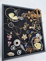 Overview of assorted vintage costume jewellery on black felt tray showing various brooches, earrings, pendants, and pins with metal and rhinestone details