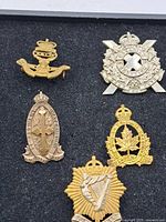 Five assorted vintage Canadian military badges arranged on black felt, showing various regimental designs and crowns.