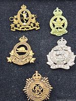Five vintage Canadian military badges arranged on black background. Includes badges with lion, beaver, horse, maple leaf, and crown motifs.
