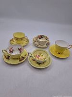 Full lot of five porcelain teacups and matching saucers in varied floral designs and colors including yellow, pink, white, and multicolor patterns