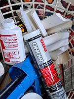 Photo showing caulking gun, adhesive tube, no-slip compound bottle and multiple white plastic handles/grips.