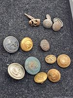 Overview of all buttons and cufflinks on black felt background showing various military insignias and patina.