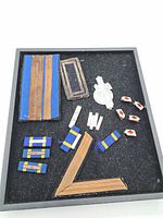 Overview of multiple WWII Italian military insignia pieces arranged on black background, including fabric ribbons, rank patches, metal pins, and badge.