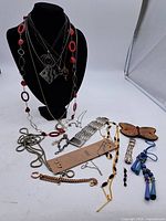 Full lot of vintage costume jewellery displayed on a black necklace stand and laid on a white surface showing necklaces, earrings, bracelets, a watch, and butterfly brooch.