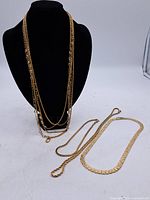 Four vintage gold-tone costume necklaces displayed on black bust and white background. One multi-strand with clear glass beads, three simpler chains laid flat.