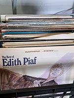 Photo showing stack of vintage vinyl records with Edith Piaf record on top, displaying album title and partial cover art.