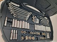 Open black plastic case with multiple chrome sockets, combo wrenches laid out in upper portion, sockets in lower portion.