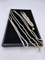 Photo showing all necklaces and bracelet on a black tray, displays different styles and bead sizes.