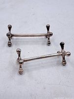 Pair of silver plated cutting utensil rests with rounded ends and horizontal bars, showing overall shape, slight tarnishing, and wear.