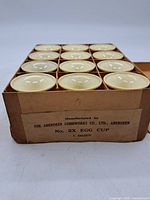 Set of 12 cream-colored vintage egg cups neatly arranged in original cardboard box labeled as manufactured by The Aberdeen Combworks Co., Ltd., Aberdeen, and marked 'No. 2X EGG CUP 1 DOZEN'.