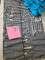 Set of silver plated flatware laid out in a grey fabric roll holder along with a turquoise cloth.