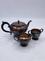 Full view of the silver plated teapot, creamer, and sugar bowl showing their shape and tarnished finish.